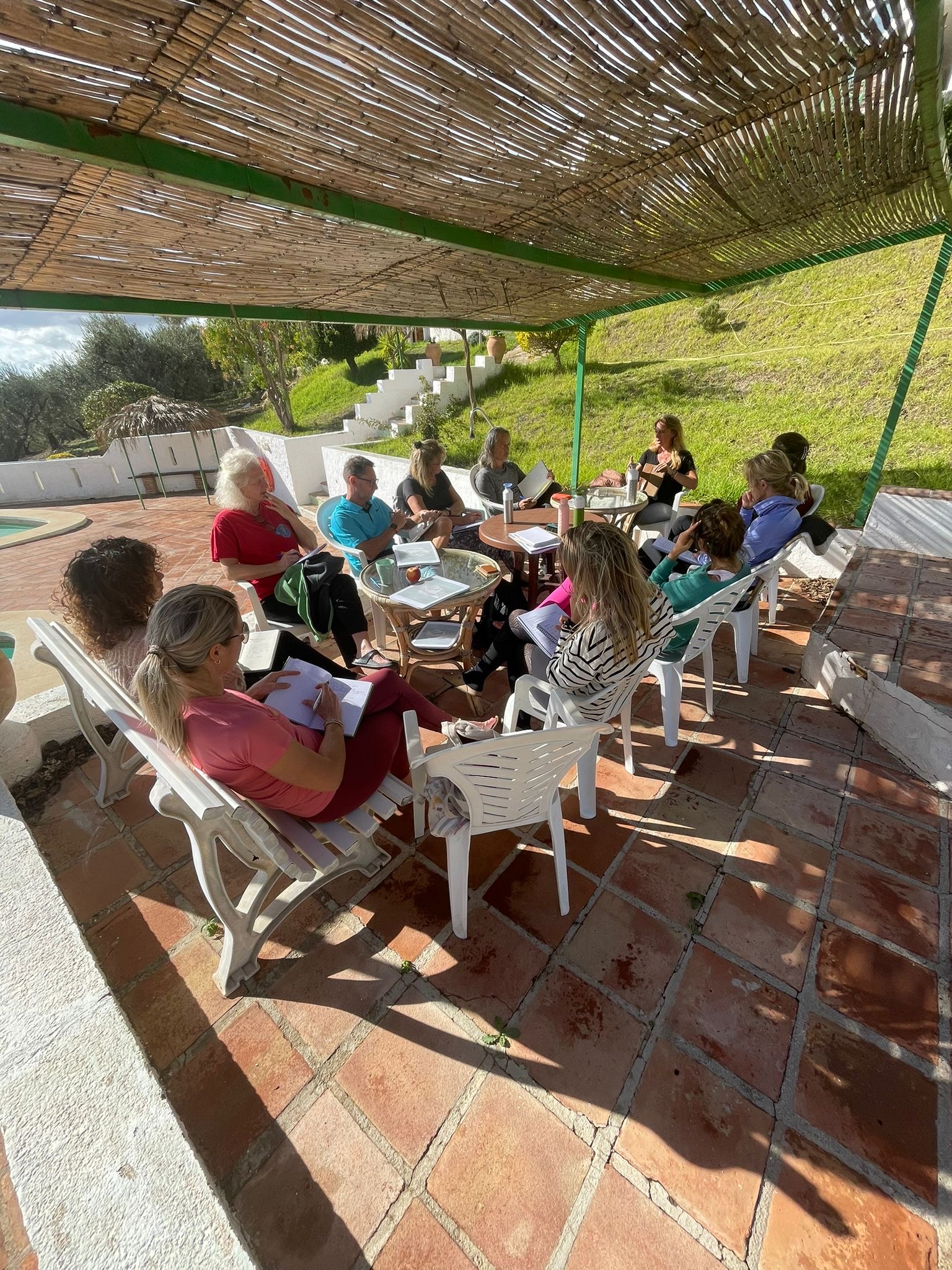 Groep cursisten tijdens een InnerPower opleiding, buiten onder een rieten overkapping, aantekeningen makend in de zon